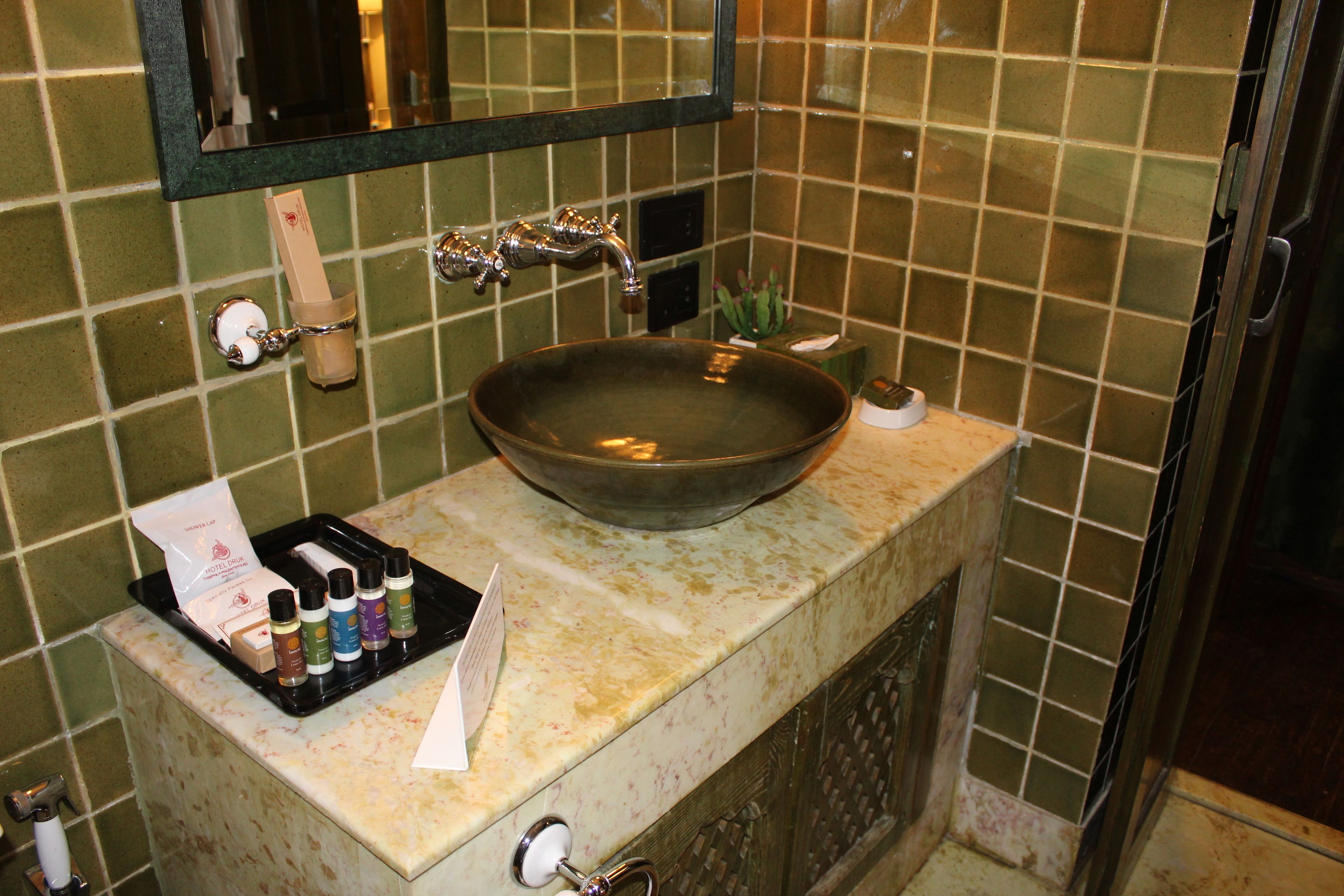 A bathroom with a large, round sink, a mirror, and a tiled wall.