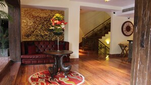 A lobby with a red sofa, a round table with a vase of flowers, and a staircase in the background. - Druk Hotel (Thimphu)