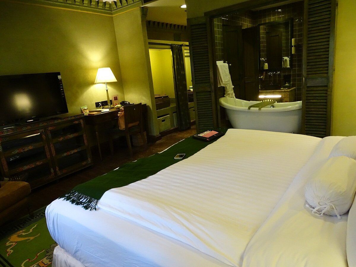 A hotel room with a large bed, a desk with a lamp, a television, and a bathroom with a bathtub.