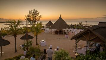 A beachside wedding setup with thatched umbrellas, white chairs, and tables arranged for guests.