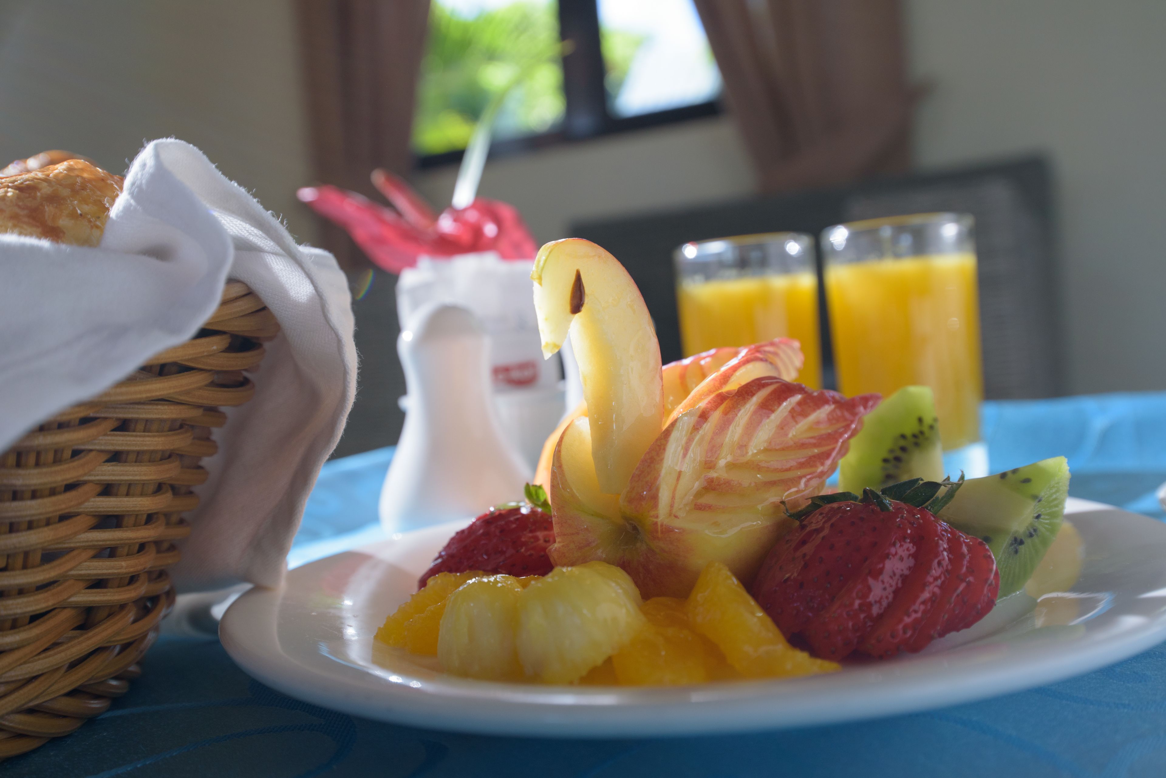 Un desayuno con una fuente de fruta, una cesta y dos vasos de zumo de naranja.