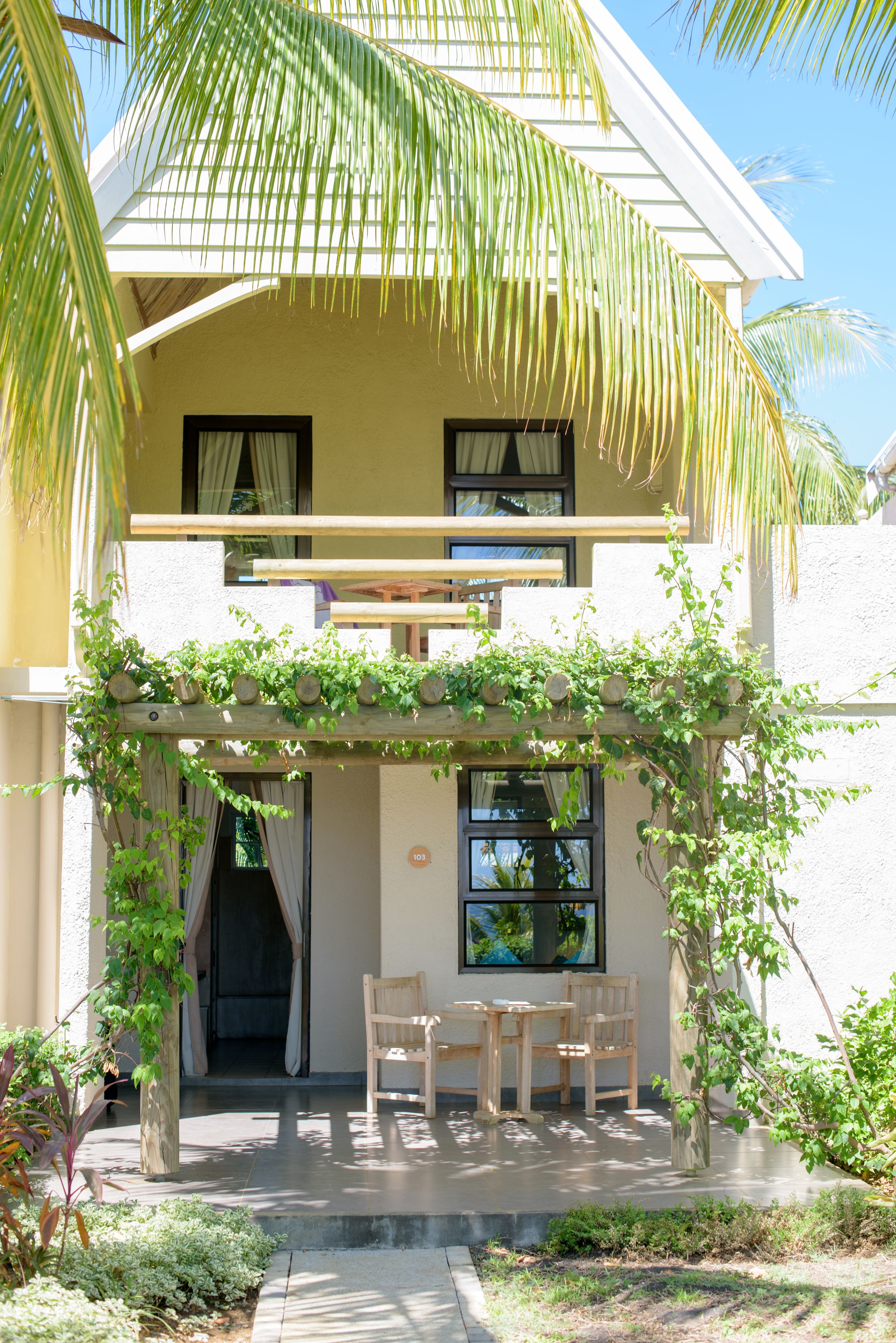 A two-story building with a covered patio area featuring a wooden pergola and a seating arrangement.