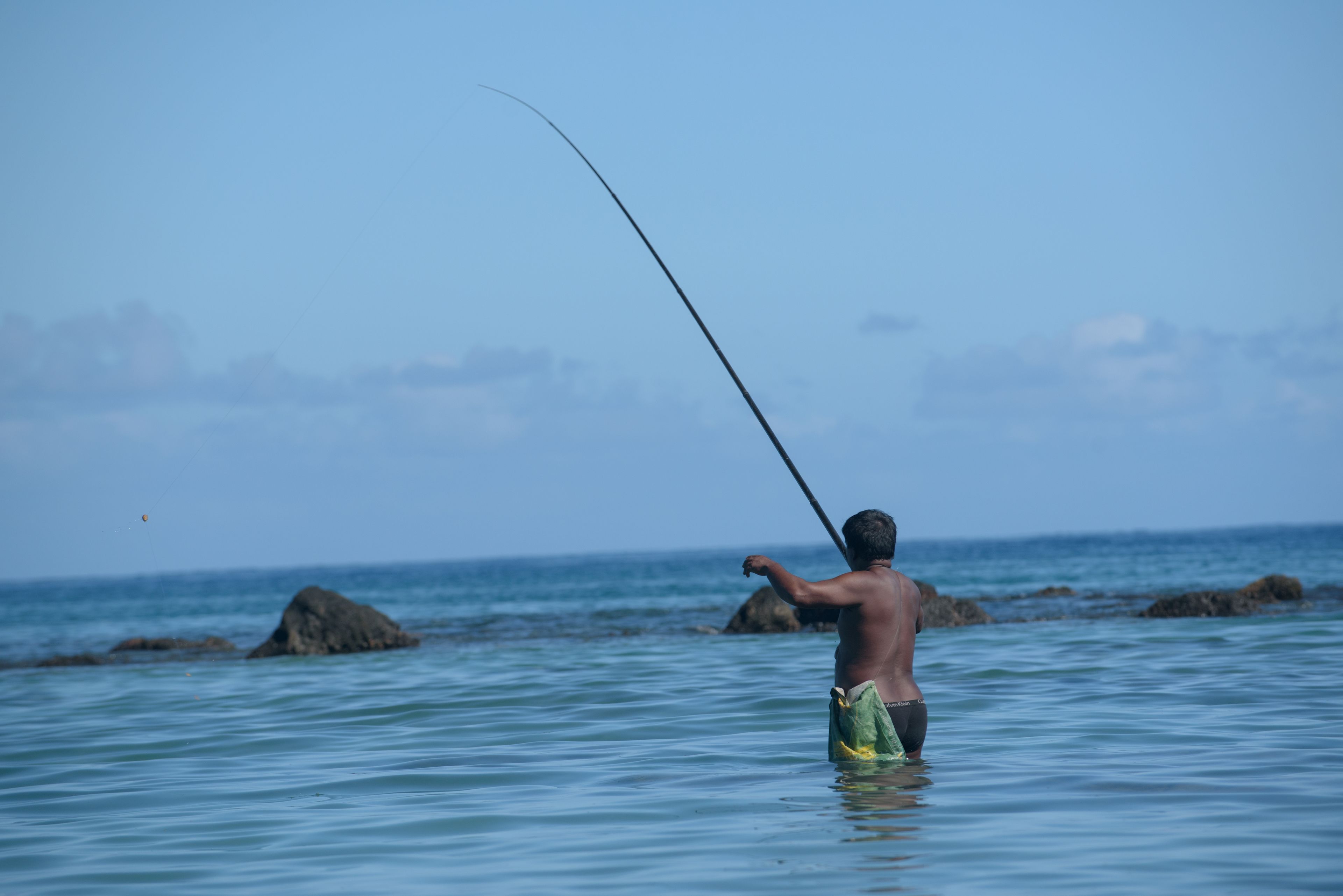 A man fishing in a body of water with rocks in the background.