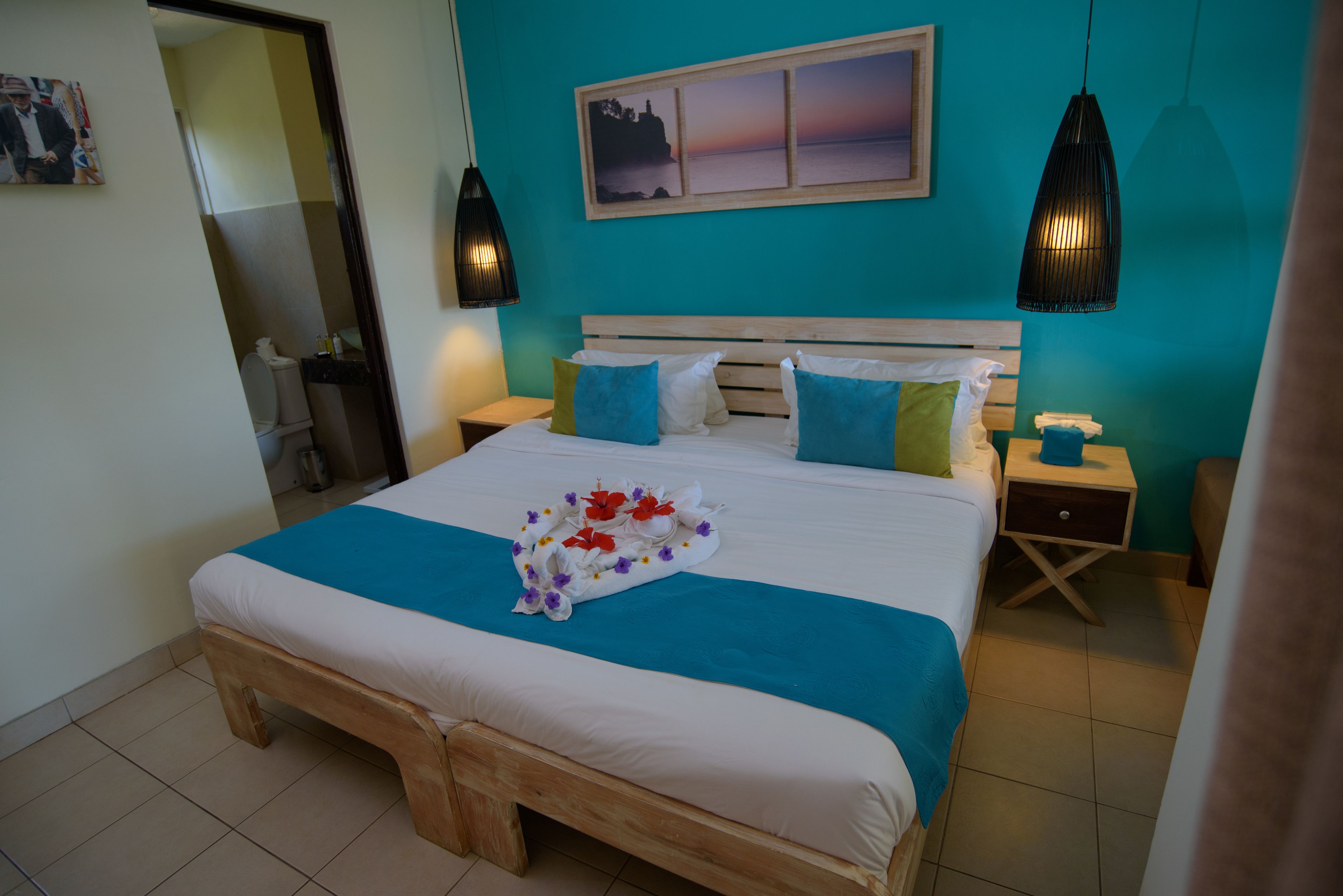 A neatly made bed with a floral arrangement, two bedside tables, a nightstand, and a wall-mounted picture.