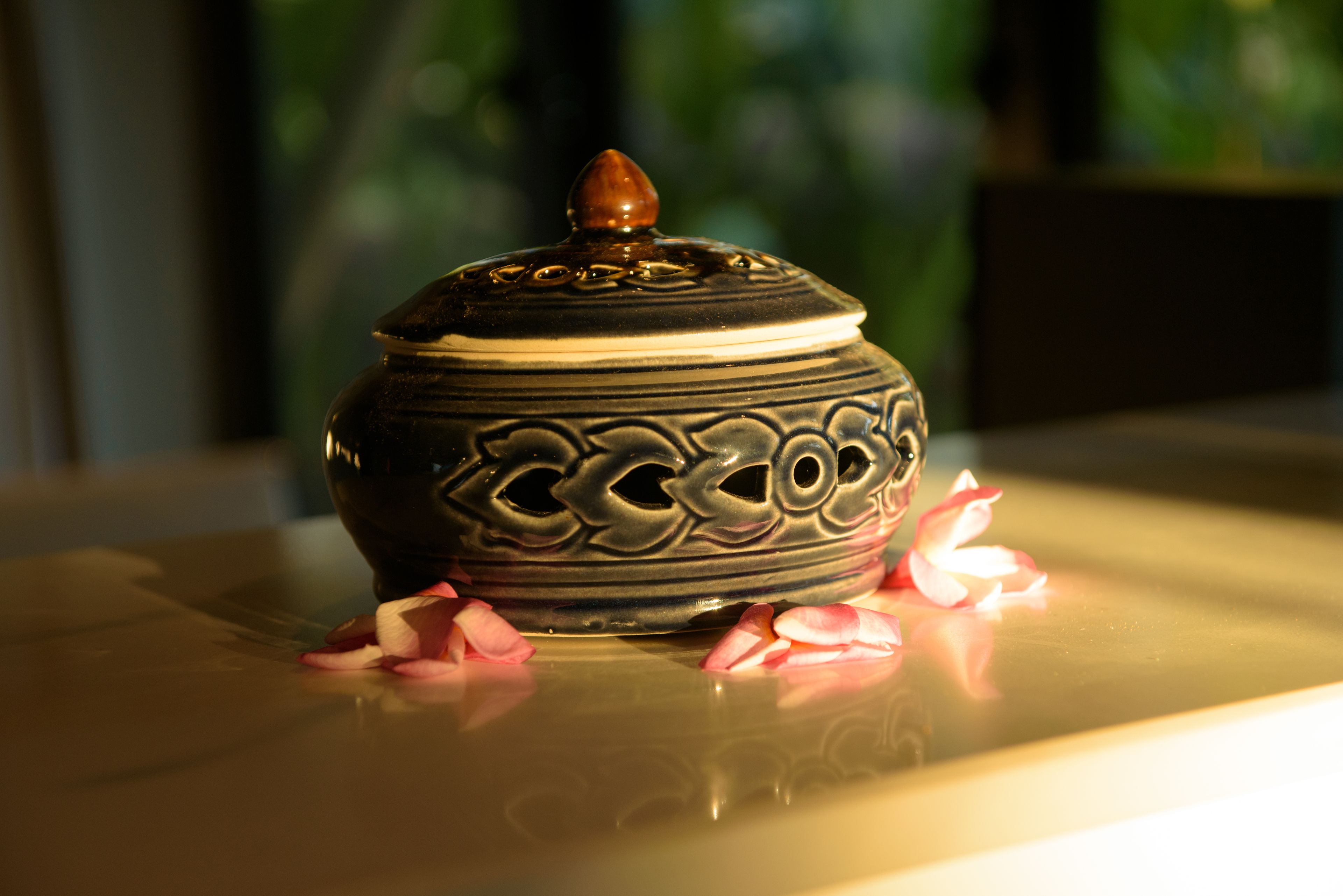 A decorative ceramic pot with a lid on a reflective surface.