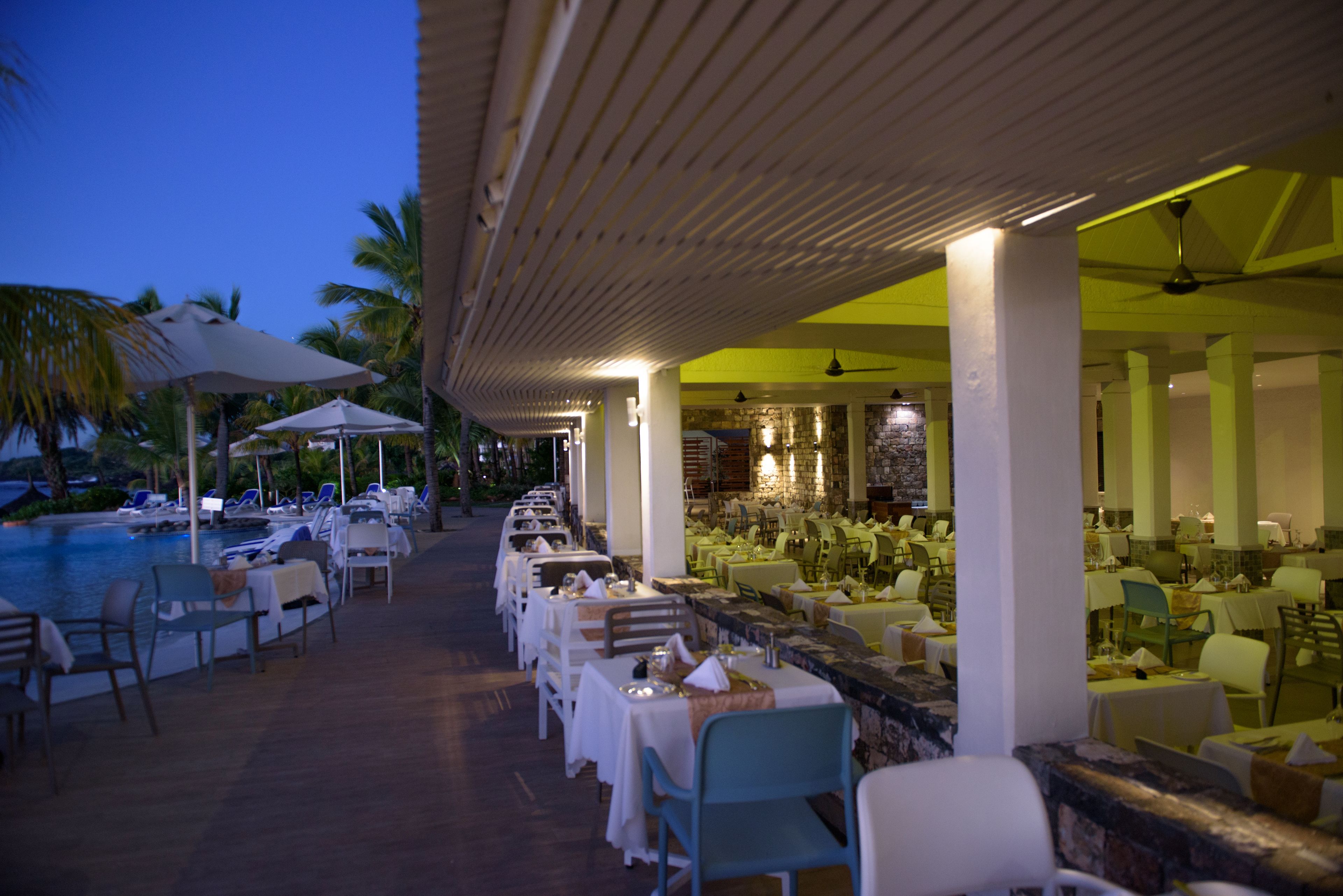 Un restaurante con terraza al aire libre que da a una piscina, con un área de patio techada con mesas y sillas.