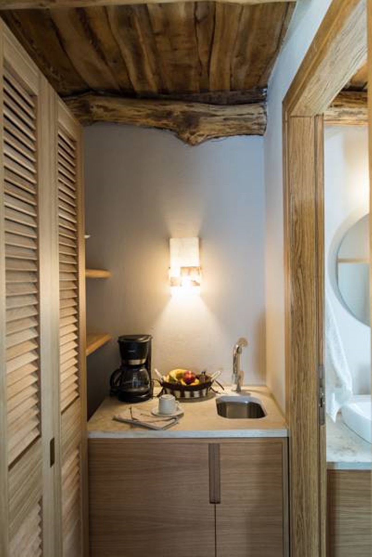 Un baño pequeño con techo de madera, un lavamanos, una cafetera y un frutero.