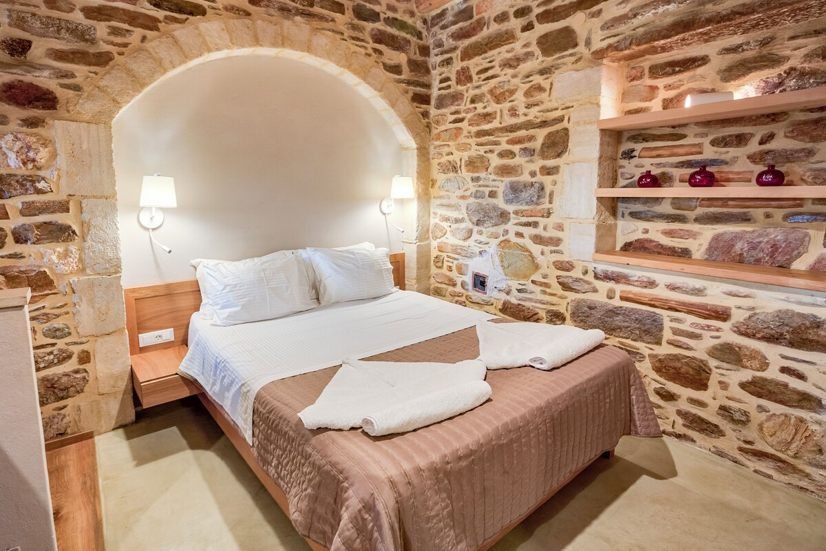 Ein Schlafzimmer mit Steinwänden, einem Bett, zwei Nachttischlampen und einem Regal mit Dekoration.