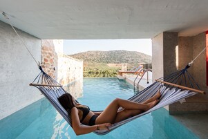 Una mujer descansando en una hamaca junto a una piscina con vistas a un paisaje montañoso.