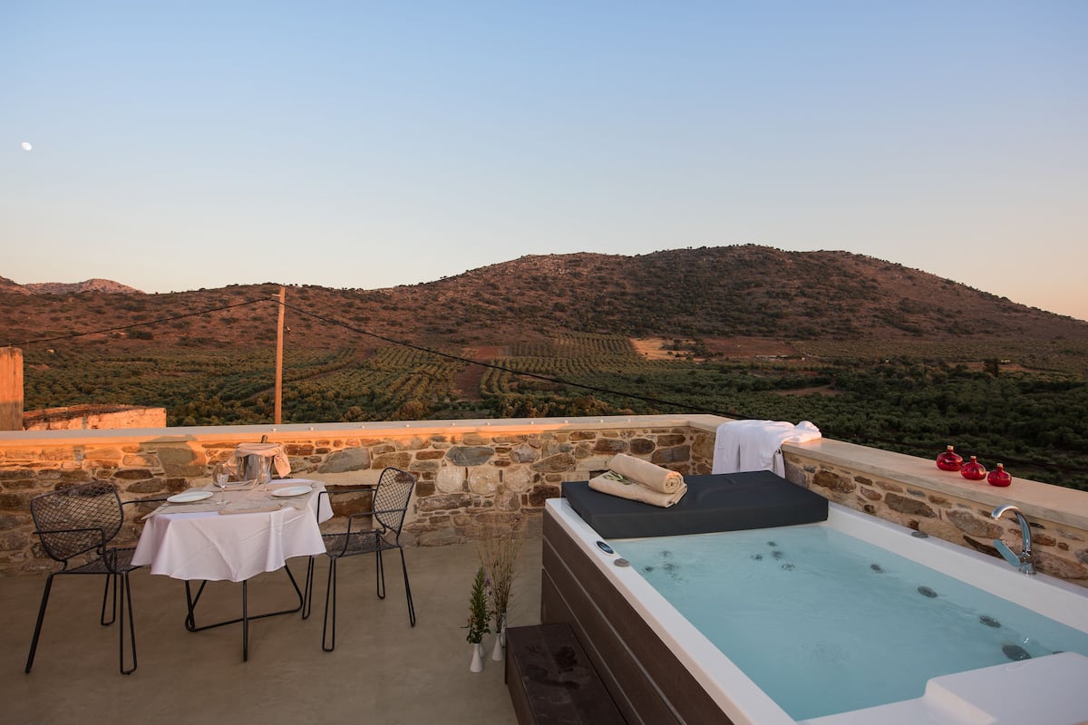 Une terrasse sur le toit aménagée avec un espace repas, un jacuzzi et une vue sur un vignoble et des collines.