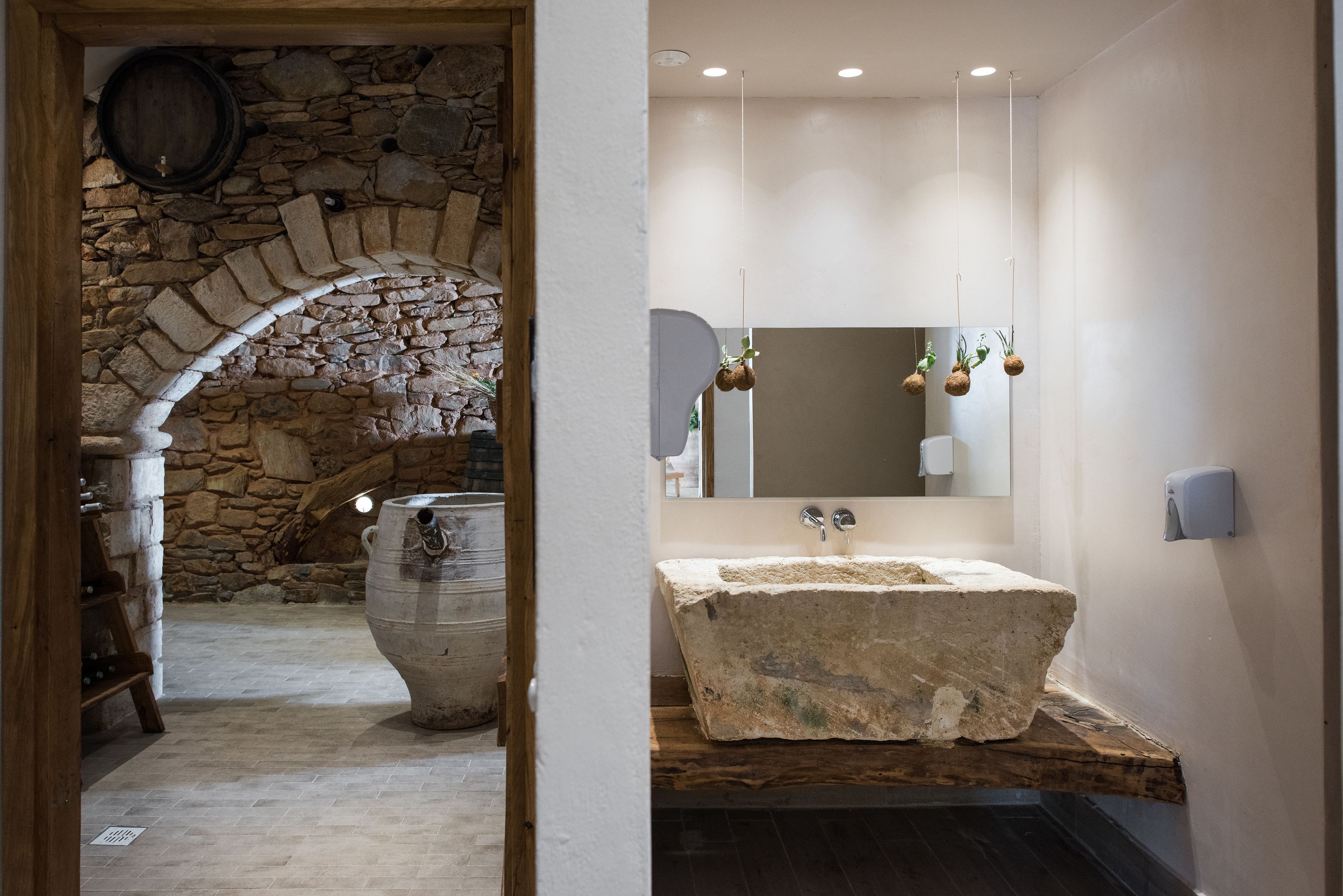A rustic bathroom with a stone sink and a large stone barrel.