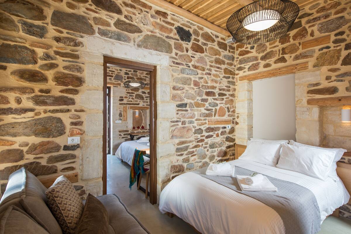 Ein Zimmer mit Stehwänden, einem Bett, einer Schlafcouch und einer Holzbalkendecke.