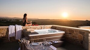 Une femme est assise près d’un muret, d’où elle peut admirer un paysage magnifique. On aperçoit un jacuzzi et une table à manger.