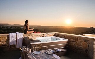 Una mujer sentada junto a un muro de piedra, con vistas a un paisaje pintoresco, una bañera de hidromasaje y una zona de comedor.