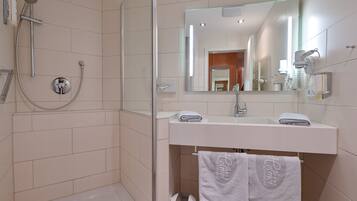 A modern bathroom with a glass-enclosed shower, a white sink with a mirror above it, and two towels hanging on a rack.