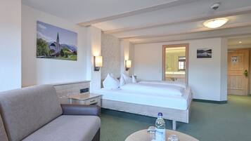 Habitación de hotel con cama, sofá, mesita de noche y una pequeña mesa redonda con una botella y un vaso.