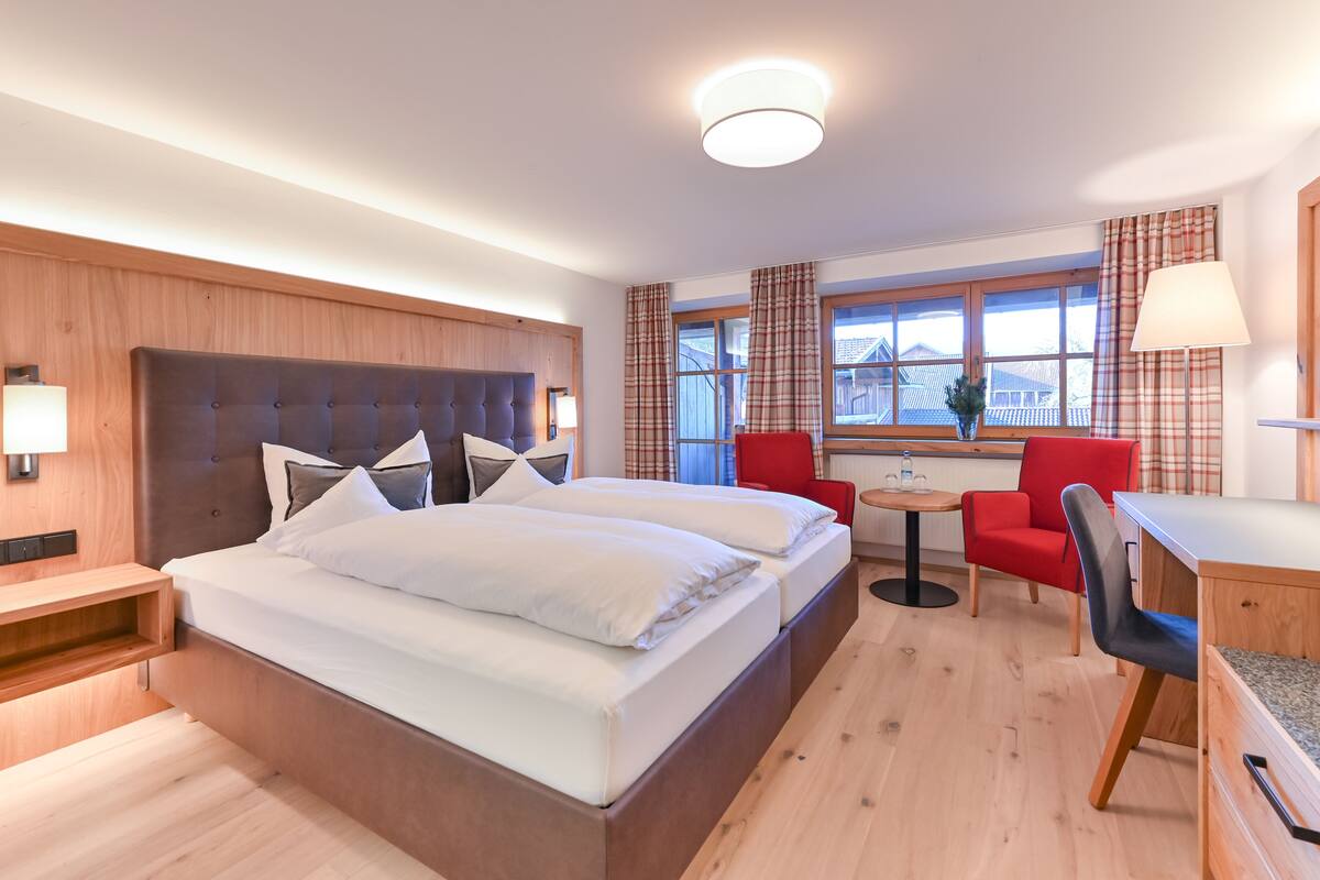 A modern hotel room with a large bed, a desk, and a chair, a small table, and a window with curtains.