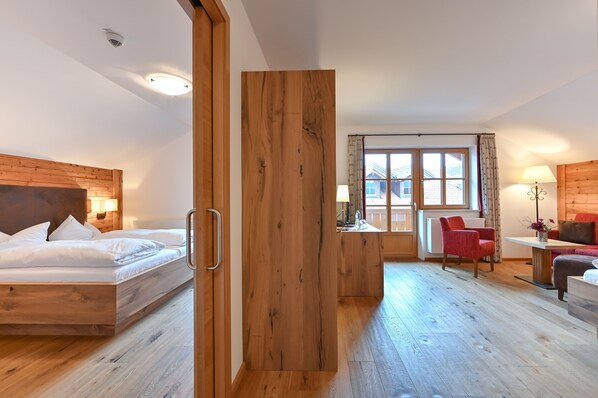Una habitación de hotel moderna con cama de cabecera de madera, separador de madera, escritorio con lámpara, una silla roja y un sofá.