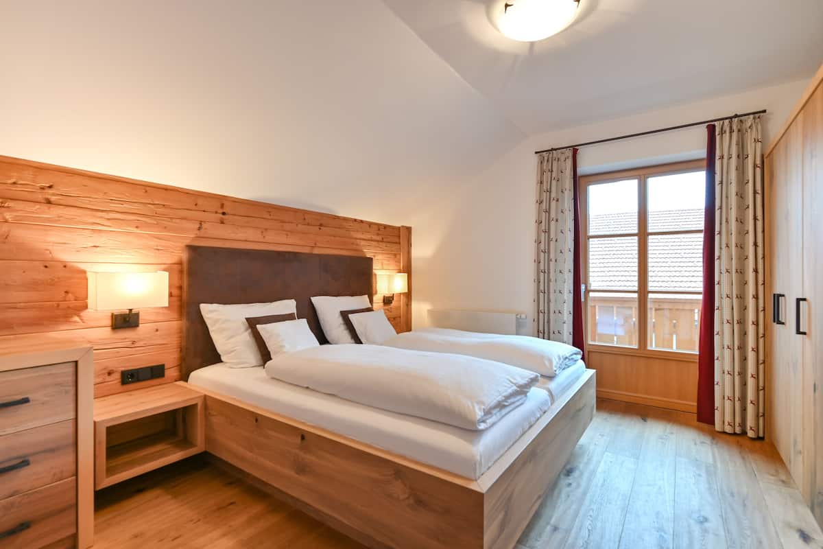 A wooden-paneled bedroom with two beds, a nightstand, and a window with curtains.