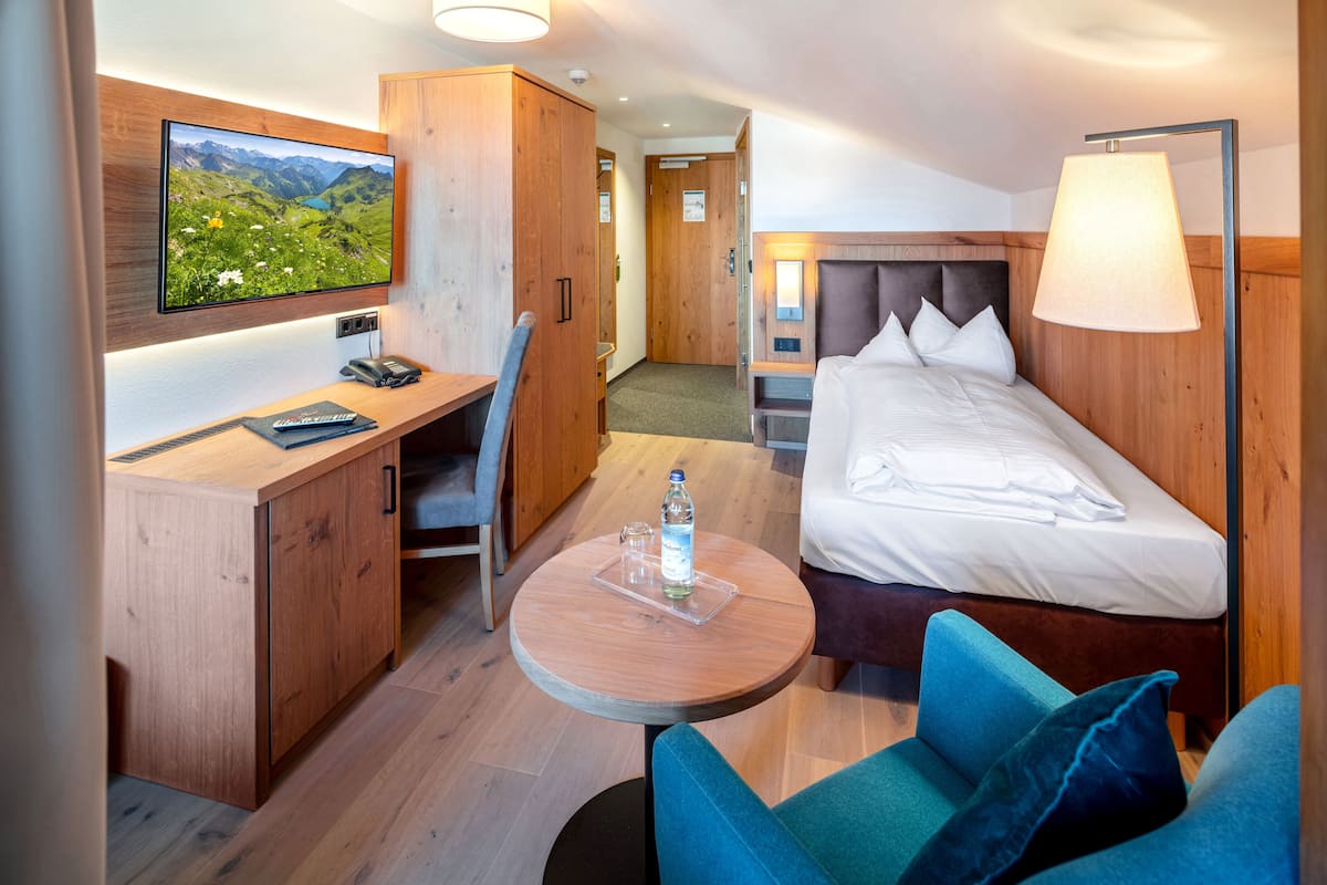 A hotel room with a bed, a desk, a chair, a round table, and a TV mounted on the wall.