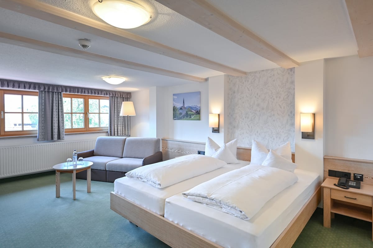 A hotel room with a large bed, a sofa, a small table, and a lamp.