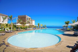 Ein Resort-Poolbereich mit mehreren Schwimmbecken, Liegestühlen und Sonnenschirmen.