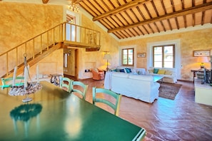 A spacious living area with a high ceiling, a staircase, and a dining table with chairs.