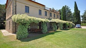 A two-story building with stone walls and a red roof. There is a covered patio area with a bench and potted plants. - Sabina (Manciano)
