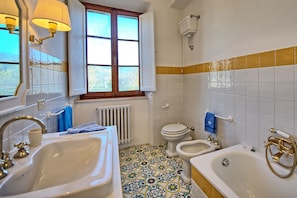 A bathroom with a sink, toilet, bidet, bathtub, and a window with a view.