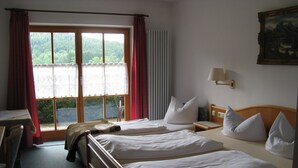 Una camera d'albergo con due letti, una scrivania e vista su una foresta dalla finestra.