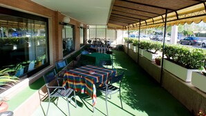 An outdoor patio with tables and chairs, a covered area, and potted plants. - Hotel Bellariva (Pescara)
