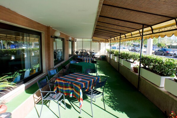 An outdoor patio with tables and chairs, a covered area, and potted plants. - Hotel Bellariva (Pescara)