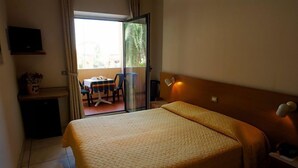 A hotel room with a bed, a desk, a chair, and a small table. There is a sliding glass door leading to an outdoor area with a table and chairs. - Hotel Bellariva (Pescara)