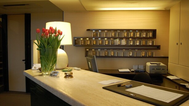 A hotel reception desk with a vase of red tulips, a lamp, and a display of framed awards on the wall. - Hotel Bellariva (Pescara)