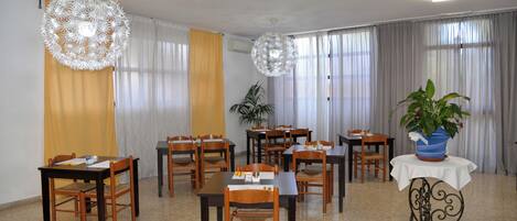 A dining area with multiple tables and chairs, a potted plant, and decorative hanging lights.