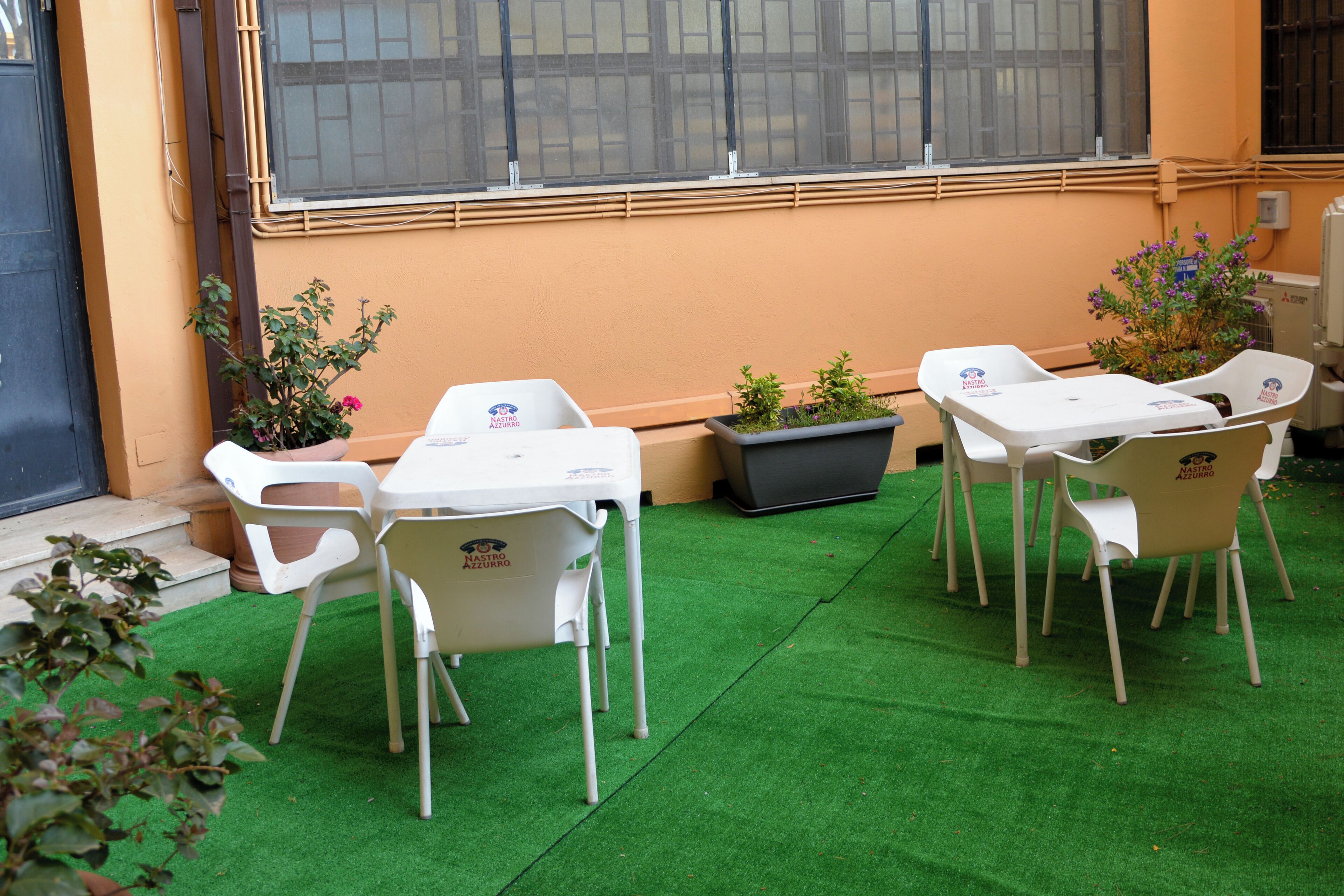 A patio area with artificial green turf, white plastic chairs, and potted plants.