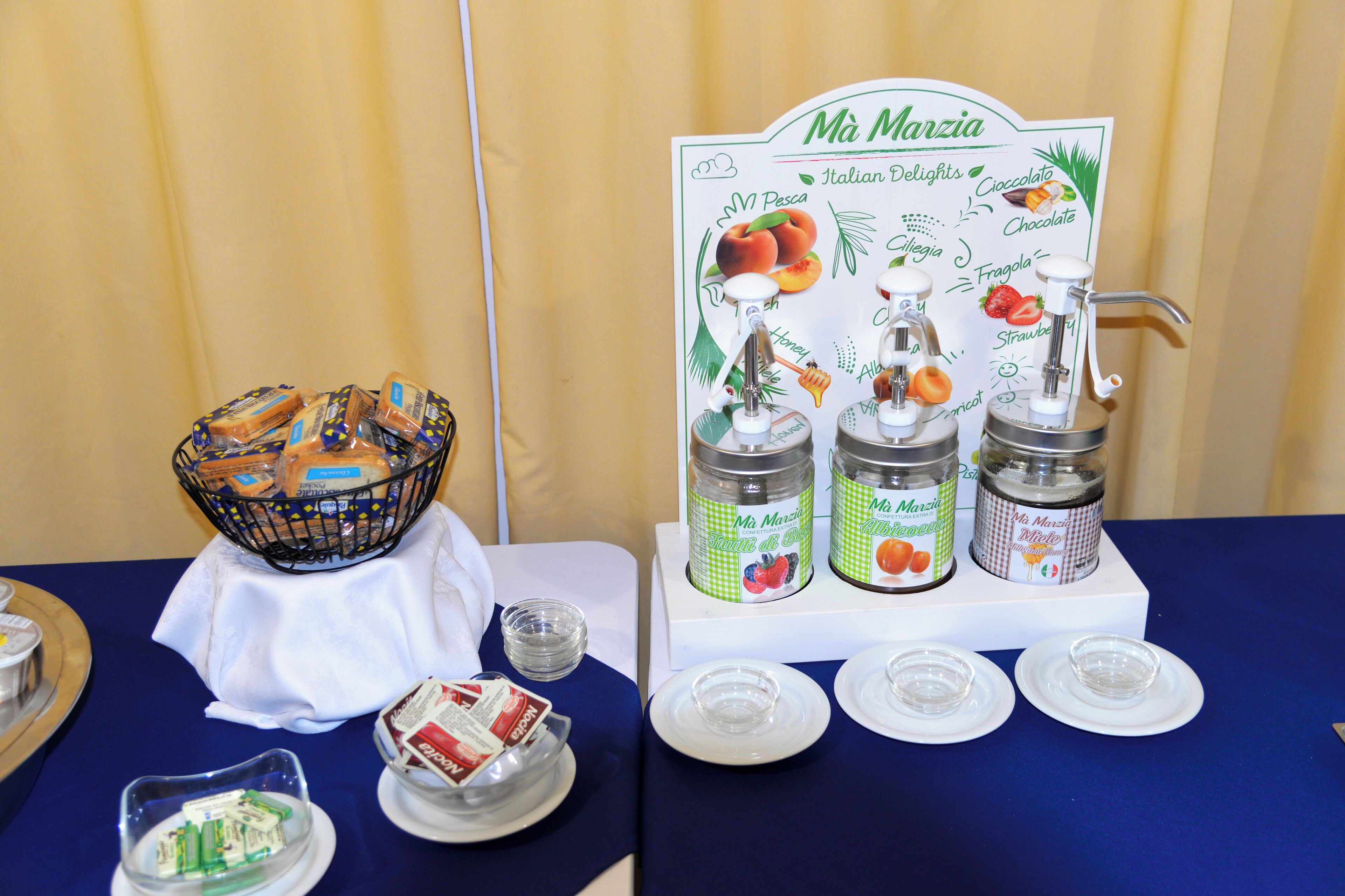 Ein reichhaltiges Buffet mit einem Schild für 'Ma Marzia Italian Delights', das Honig, Mandel und Aprikose zeigt.