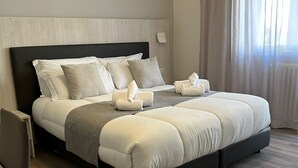 A modern hotel room with a large bed, a wooden headboard, and a view of a cityscape through sheer curtains. - Il Romitello  (Rome)