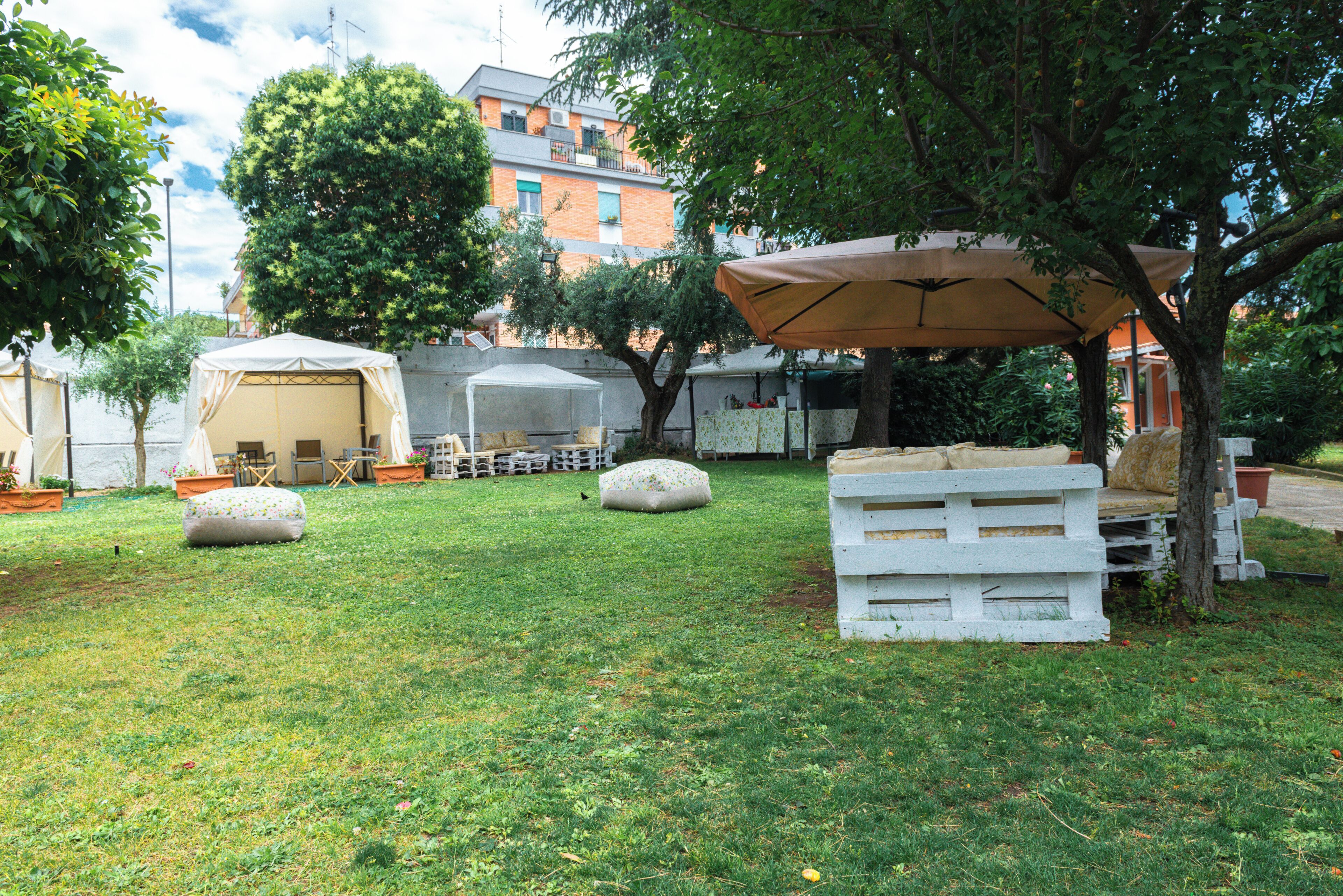 Un'area esterna con tavoli e sedie, una zona salotto coperta e un edificio sullo sfondo.