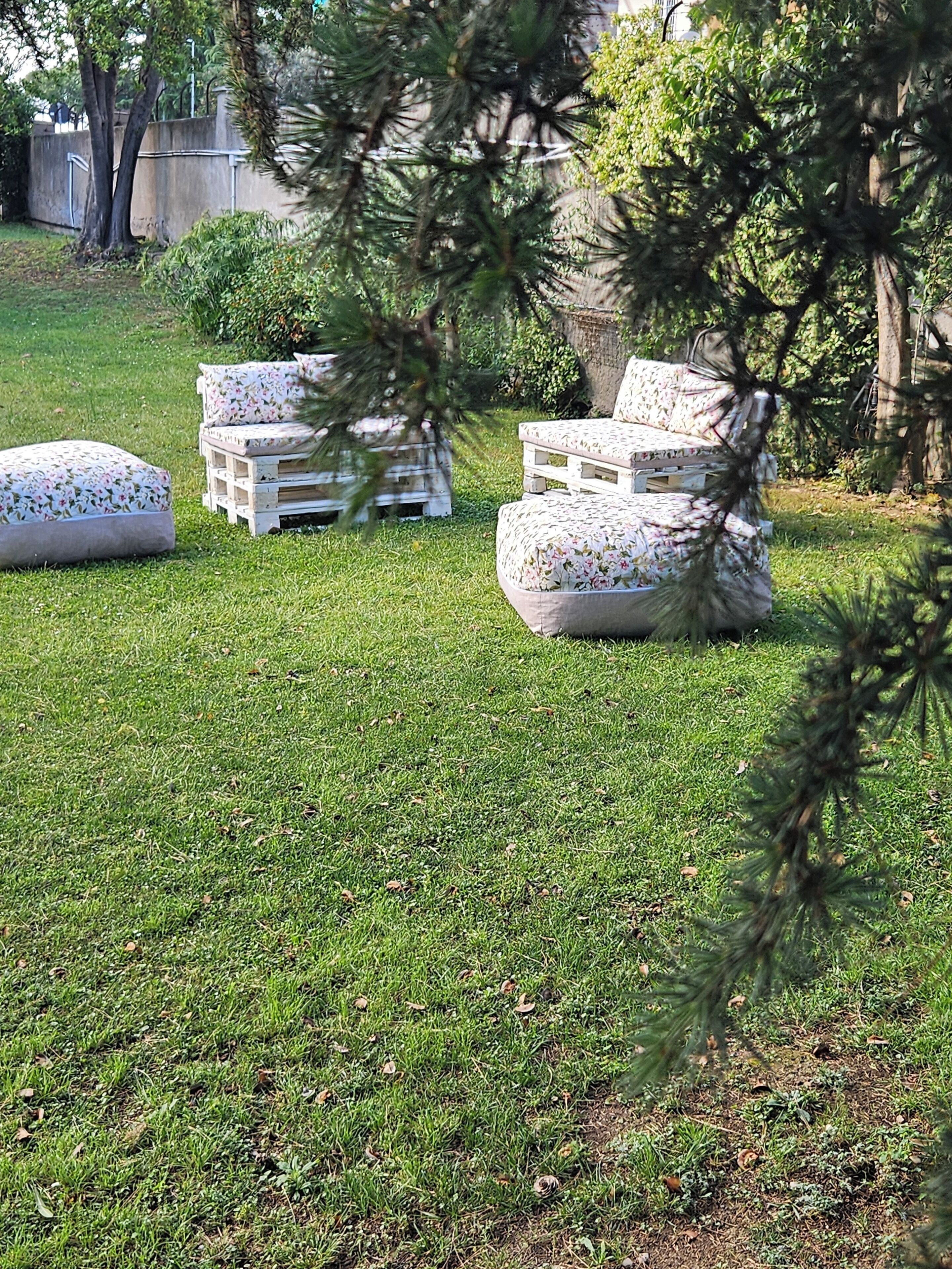 Outdoor seating with floral cushions and wooden benches on a grassy lawn.