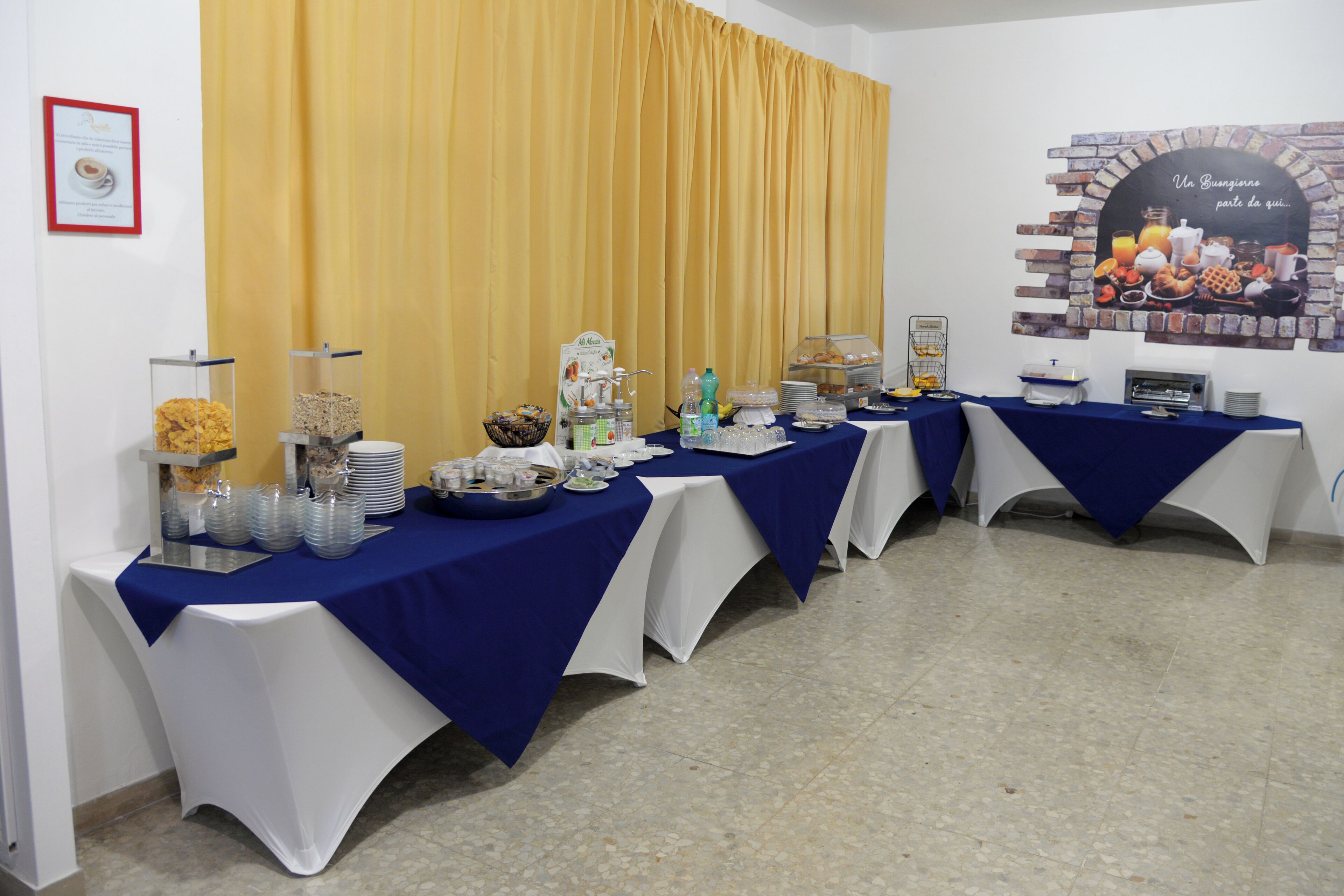 A buffet setup with multiple tables covered in blue tablecloths, featuring various food and drink items.
