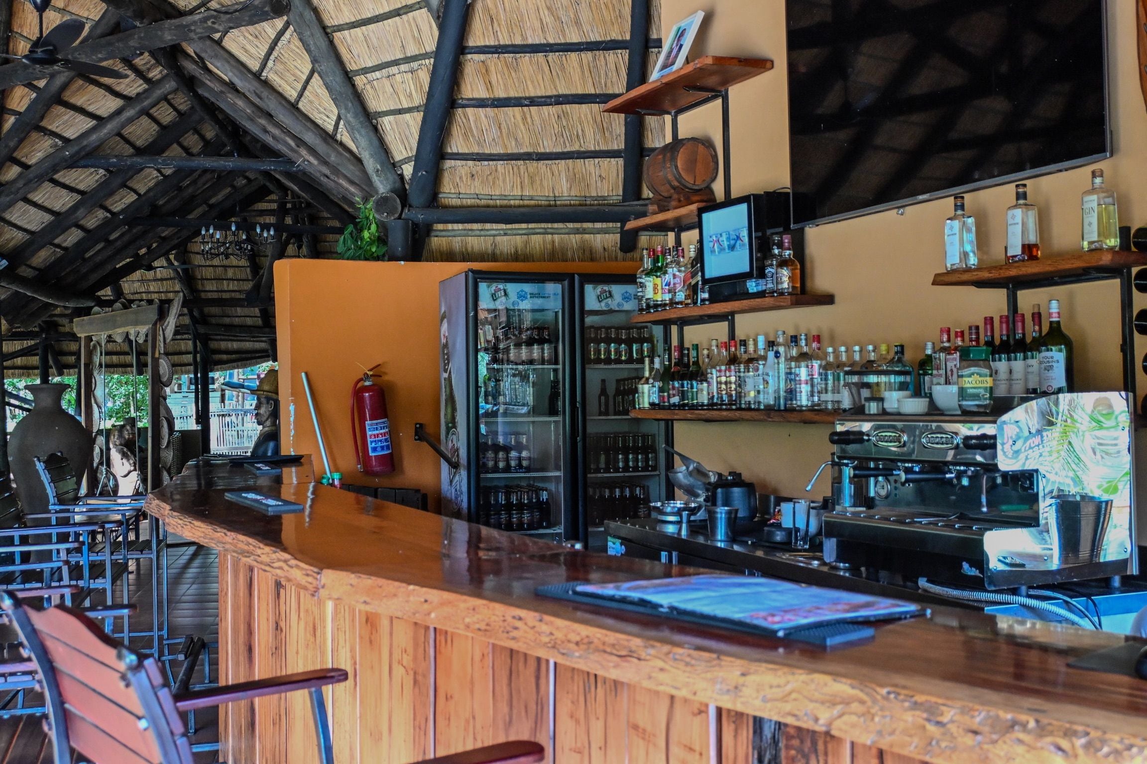 Angolo bar con bancone in legno, scaffali pieni di bottiglie, un frigorifero e una macchina da caffè.