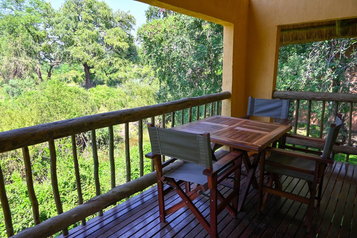 A wooden deck with a table and chairs, overlooking a lush green forest.