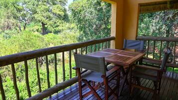 A wooden deck with a table and chairs, overlooking a lush green forest.