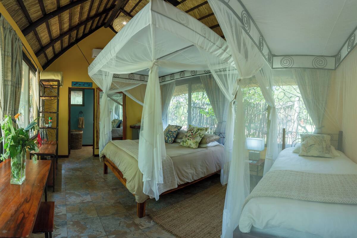 A room with a four-poster bed, a wooden desk, and a bench.