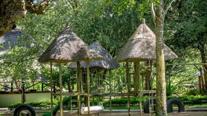 A playground with thatched-roof play structures and a slide. - Maramba River Lodge (Livingstone)