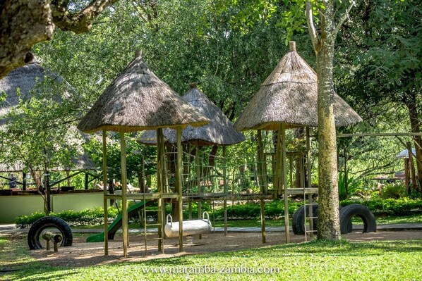 Un parque infantil con estructuras de juegos de techo de paja y un tobogán.