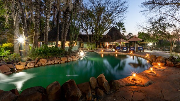 A serene outdoor pool area with a stone pathway, seating, and a gazebo. - Maramba River Lodge (Livingstone)