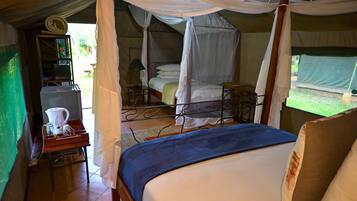 Alojamiento tipo tienda con una cama, una mesa con hervidor, y un estante pequeño con libros y una lámpara.