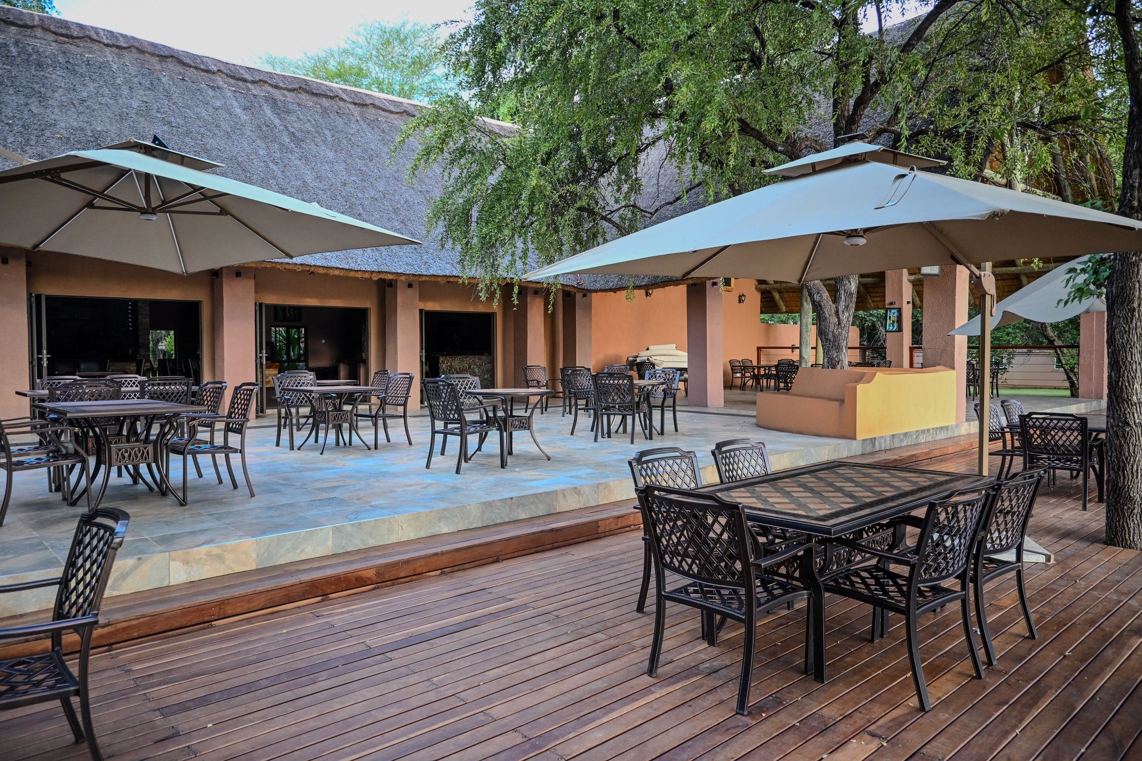 An outdoor patio area with tables and chairs, umbrellas, and a thatched-roof building.